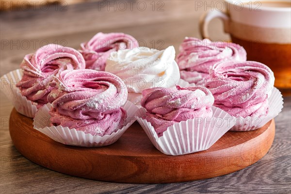 Pink and white marshmallows (zephyr) on a round wooden board with cup of coffee on a gray wooden