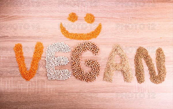 Word Vegan with a smile made of lentils, buckwheat, beans, rice and chickpeas on a wooden
