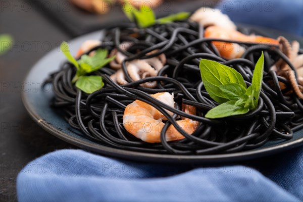 Black cuttlefish ink pasta with shrimps or prawns and small octopuses on black concrete background