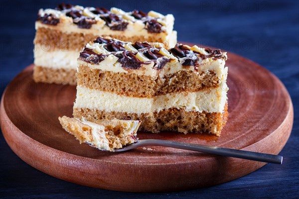 A piece of cake with milk and butter cream cutted with spoon on a wooden kitchen board, close up,