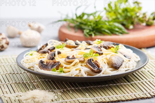 Rice noodles with champignons mushrooms, egg sauce and oregano on blue ceramic plate on a gray