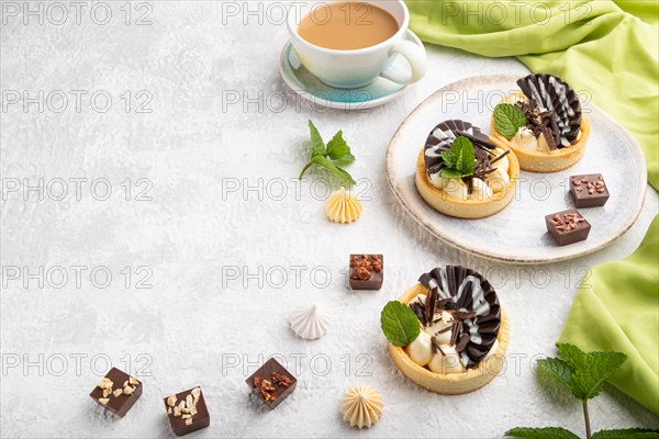 Sweet tartlets with chocolate and cheese cream with cup of coffee on a gray concrete background and