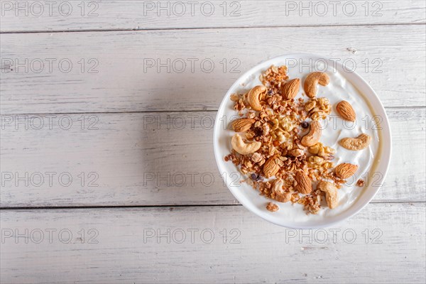 White plate with greek yogurt, granola, almond, cashew, walnuts on white wooden background. top
