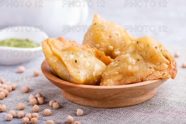 Traditional indian food samosa in wooden plate with mint chutney on a gray concrete background.