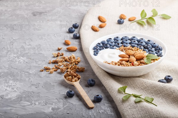 Yoghurt with blueberry, granola and almond in white plate with wooden spoon on gray concrete