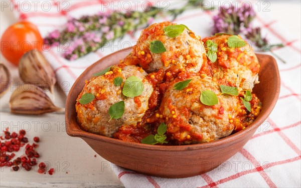 Pork meatballs with tomato sauce, oregano leaves, spices and herbs in clay bowl on a white wooden