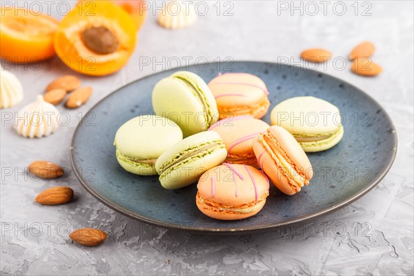 Orange and green macarons or macaroons cakes on blue ceramic plate on a gray concrete background.