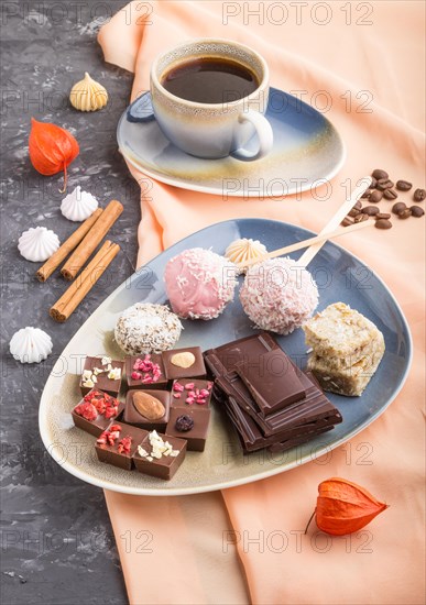 A pieces of homemade chocolate with coconut candies and a cup of coffee on a black concrete