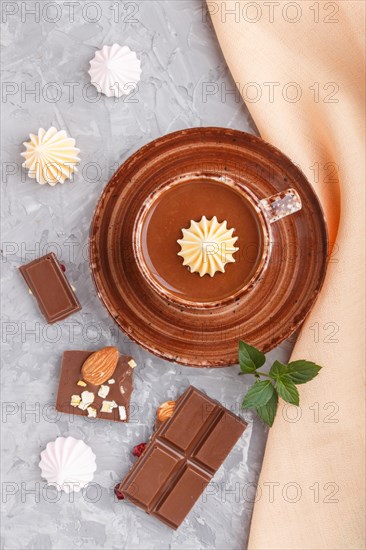 Cup of hot chocolate and pieces of milk chocolate with almonds on a gray concrete background with