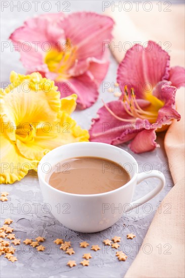 Yellow anf purple day-lilies cup of coffee on a gray concrete background, with orange textile.