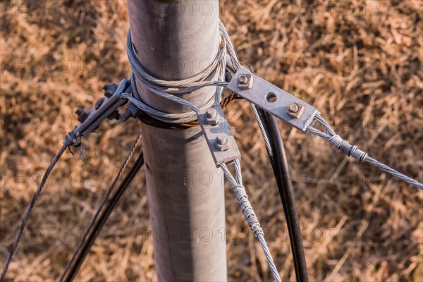 Top down view of wire cables attached to metal pole with brown grass blurred in background in South