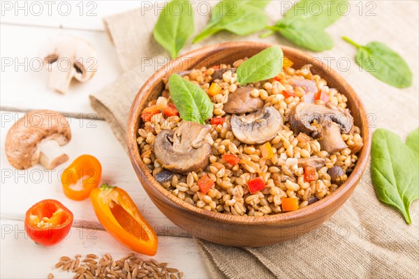 Spelt (dinkel wheat) porridge with vegetables and mushrooms in wooden bowl on a white wooden