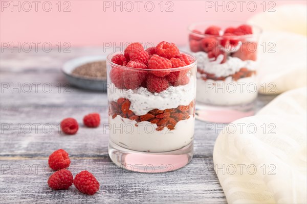Yogurt with raspberry, goji berries and chia seeds in glass on gray wooden background and linen