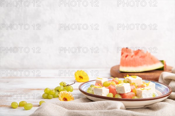 Vegetarian salad with watermelon, feta cheese, and grapes on blue ceramic plate on white wooden