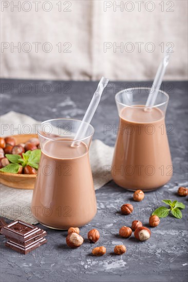 Organic non dairy hazelnut chocolate milk in glass and wooden plate with hazelnuts on a black