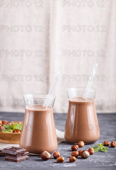 Organic non dairy hazelnut chocolate milk in glass and wooden plate with hazelnuts on a black