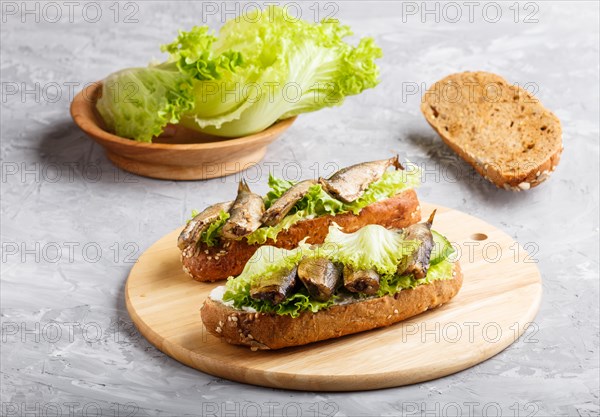 Sprats sandwiches with lettuce and cream cheese on wooden board on a gray concrete background. side