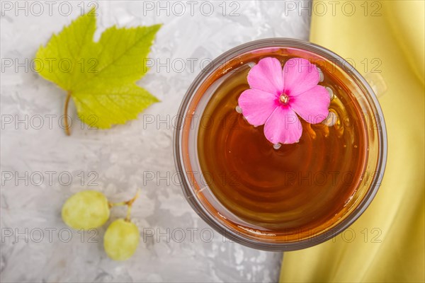 Glass of green grape juice with green textile and pink flower on a gray concrete background.