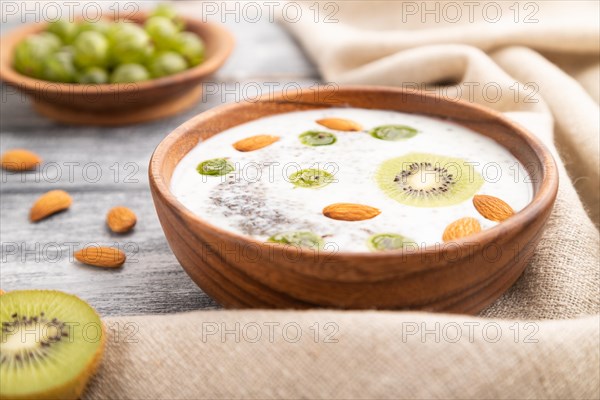 Yogurt with kiwi, gooseberry, chia and almonds in wooden bowl on gray wooden background and linen