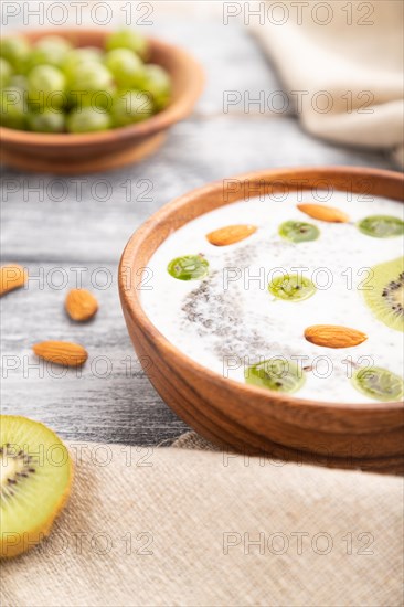 Yogurt with kiwi, gooseberry, chia and almonds in wooden bowl on gray wooden background and linen