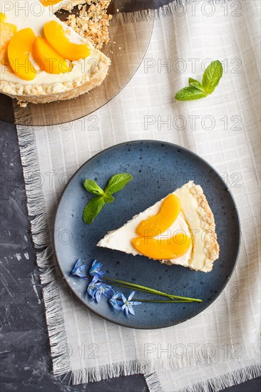 A piece of peach cheesecake on a blue ceramic plate with blue flowers on a linen napkin on a black