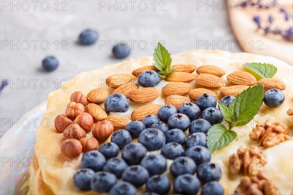 Homemade layered Napoleon cake with milk cream. Decorated with blueberry, almonds, walnuts,