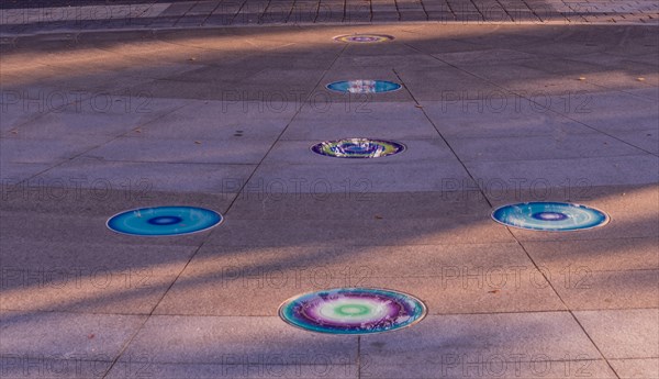 Arrow of round glass tiles of blue, purple, yellow and white inlaid in concrete sidewalk in public