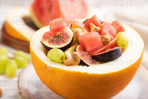 Vegetarian fruit salad of watermelon, grapes, figs, pear, orange, cashew on white wooden background