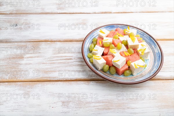 Vegetarian salad with watermelon, feta cheese, and grapes on blue ceramic plate on white wooden