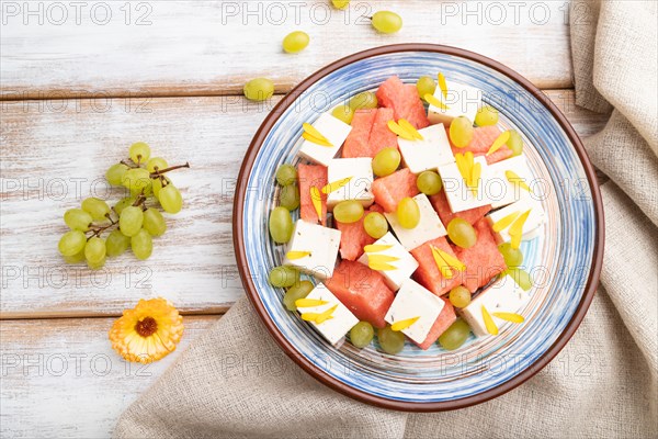 Vegetarian salad with watermelon, feta cheese, and grapes on blue ceramic plate on white wooden