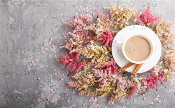 Pink and red astilbe flowers and a cup of coffee on a gray concrete background. Morninig, spring,