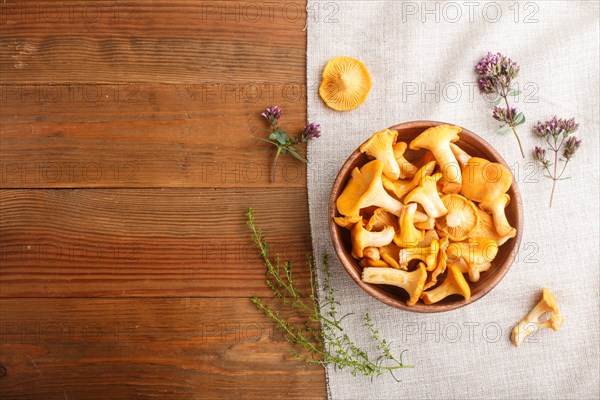 Chanterelle mushrooms in wooden bowl and spice herbs on wooden background with linen textile. top