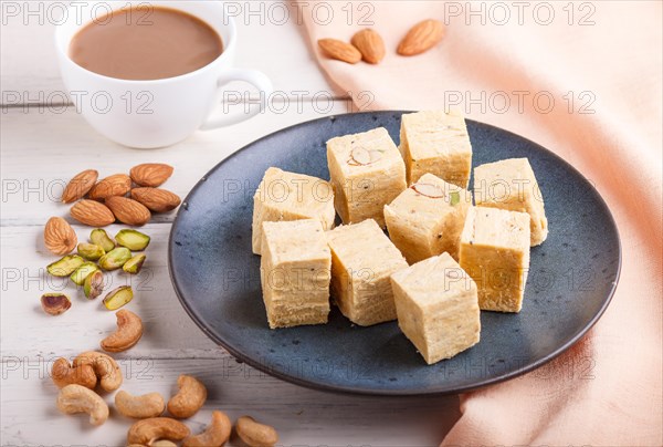 Traditional indian candy soan papdi in a blue ceramic plate with almond, pistache, cashew and a cup