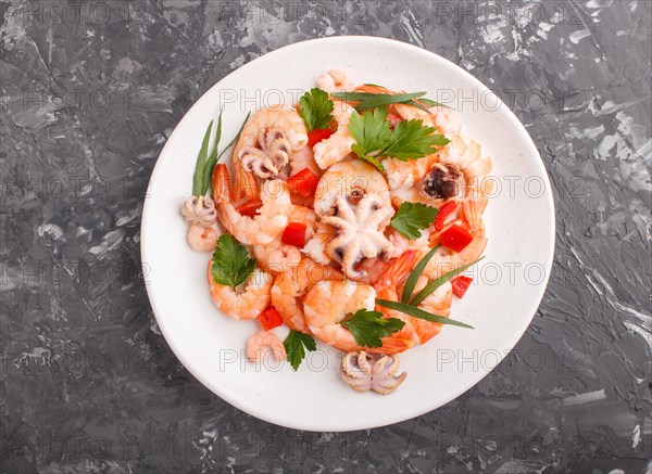 Boiled shrimps or prawns and small octopuses with herbs on white ceramic plate on a black concrete