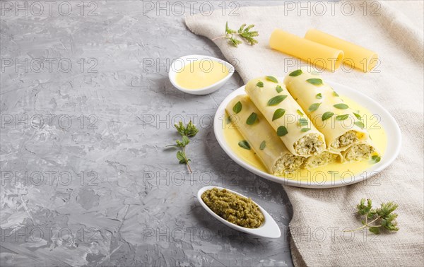 Cannelloni pasta with egg sauce, cream cheese and oregano leaves on a gray concrete background with