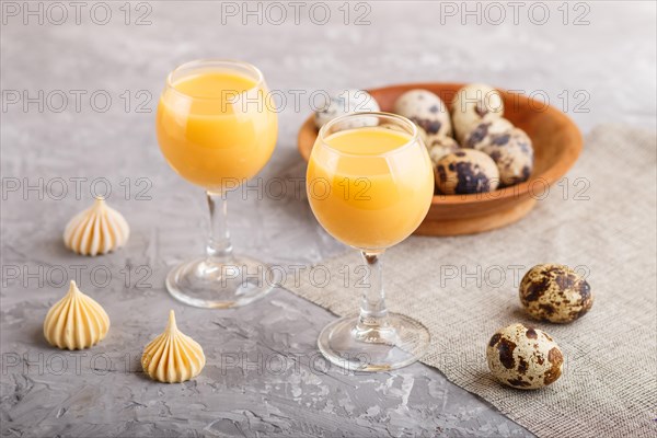 Sweet egg liqueur in glass with quail eggs and meringues on a gray concrete background. Side view,
