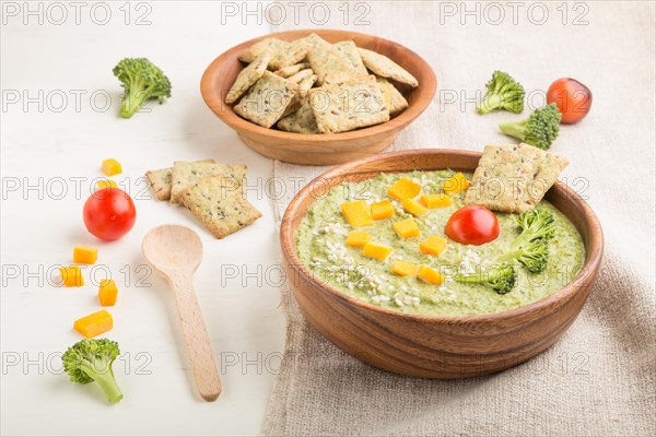 Green broccoli cream soup with crackers and cheese in wooden bowl on a white wooden background and