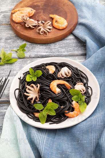 Black cuttlefish ink pasta with shrimps or prawns and small octopuses on gray wooden background and
