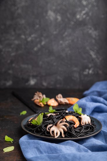 Black cuttlefish ink pasta with shrimps or prawns and small octopuses on black concrete background
