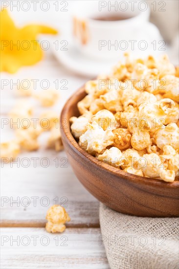Popcorn with caramel in wooden bowl and a cup of coffee on a white wooden background and linen