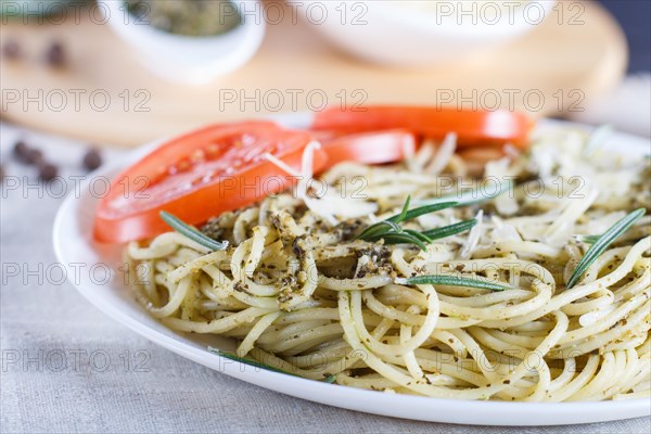 Spaghetti pasta with pesto sauce, tomatoes and cheese on a linen tablecloth. close up, selective