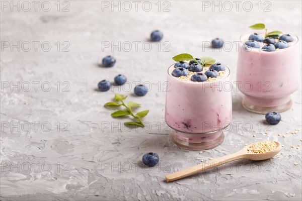 Yoghurt with blueberry and sesame in a glass and wooden spoon on gray concrete background. side