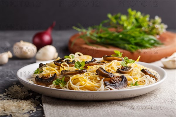 Rice noodles with champignons mushrooms, egg sauce and oregano on white ceramic plate on a black