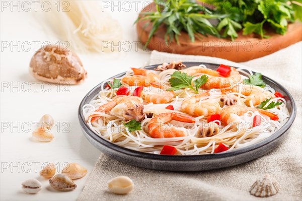 Rice noodles with shrimps or prawns and small octopuses on gray ceramic plate on a white wooden