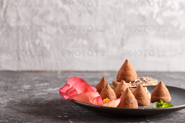Chocolate truffle on blue ceramic plate decorated with rose petals on black concrete background.