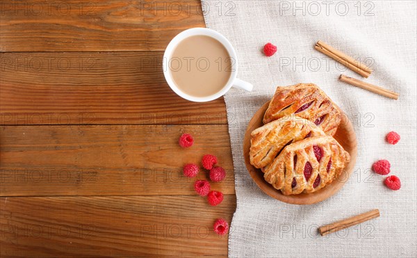 Puff pastry buns with strawberry jam on wooden background with linen textile and a cup of coffee.
