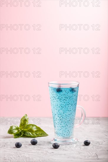 Glass of blueberry blue colored drink with basil seeds on a gray and pink background. Morninig,