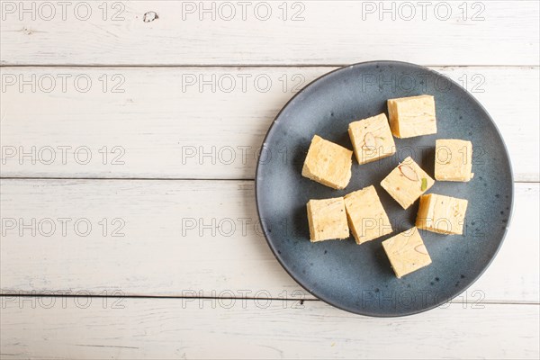 Traditional indian candy soan papdi in a blue ceramic plate with almond and pistache on a white