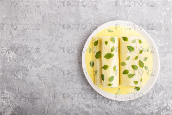 Cannelloni pasta with egg sauce, cream cheese and oregano leaves on a gray concrete background. top