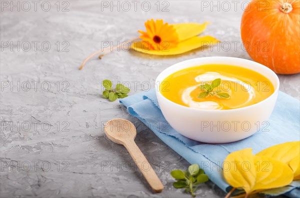 Traditional pumpkin cream soup with in white bowl on a gray concrete background with blue napkin.